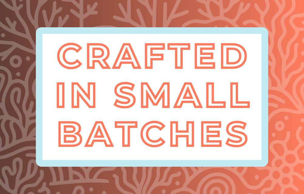 Text 'Crafted in Small Batches' on a white background, surrounded by a soft blue frame and a coral-toned and coral-themed backdrop, highlighting the artisan and small-batch blending process for artisan tea