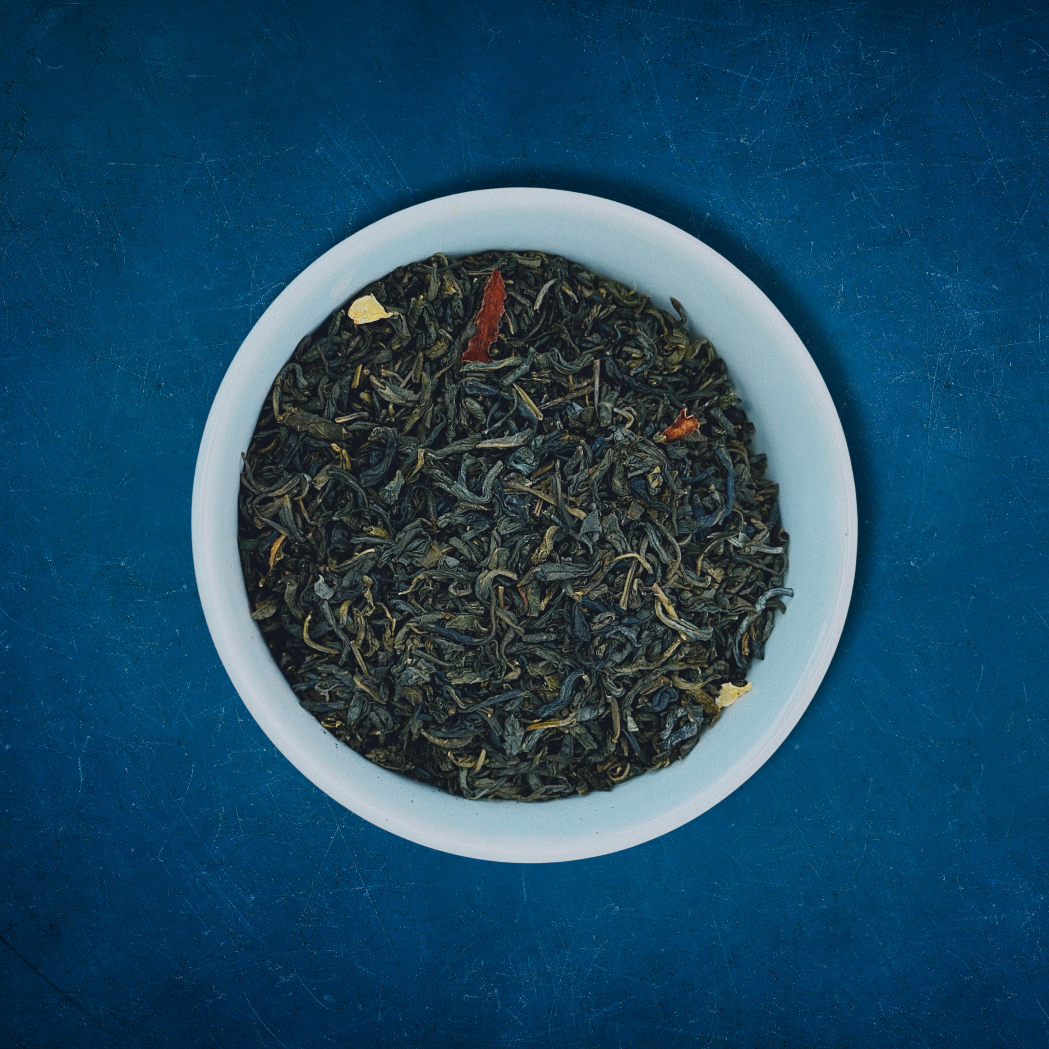 Close-up of Gulfstream Glow loose-leaf jasmine green tea in a white bowl on a blue background by Wonder Waves Coffee