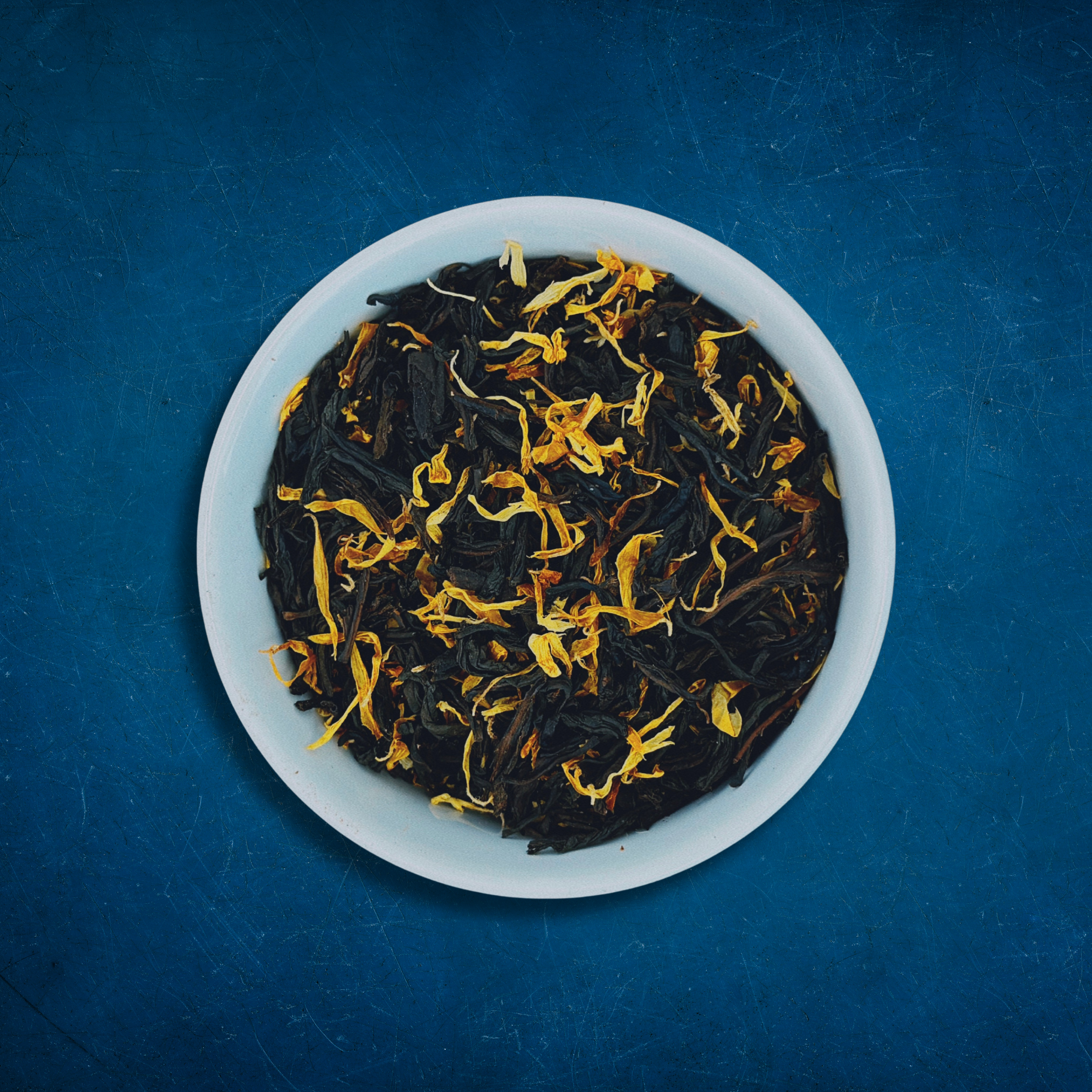 Close-up of Tropical Tides loose-leaf Mango black tea tea in a white bowl on a blue background by Wonder Waves Coffee