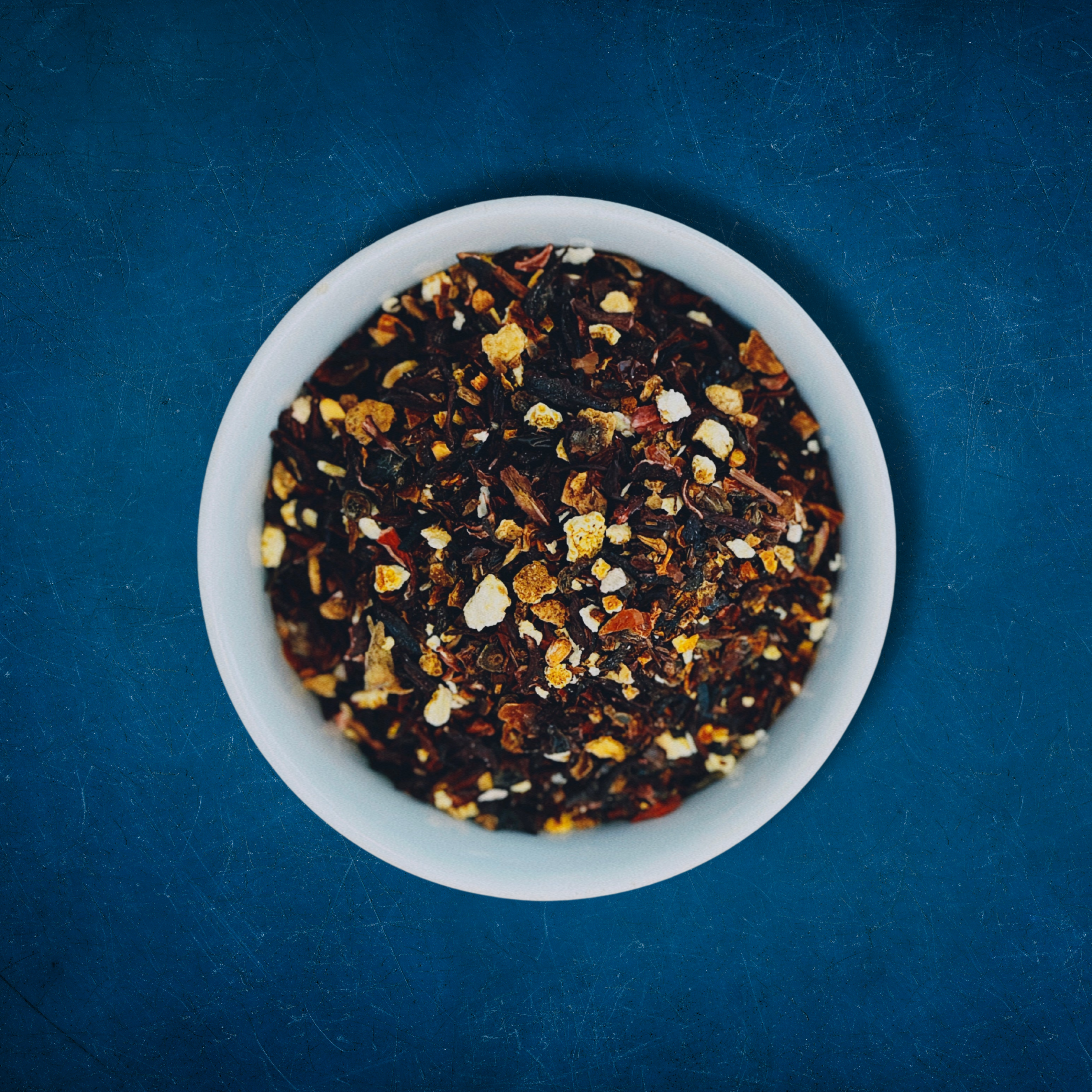 Close-up of Horizon Hues loose-leaf Hibiscus Berry Rooibos caffeine-free tea in a white bowl on a blue background by Wonder Waves Coffee