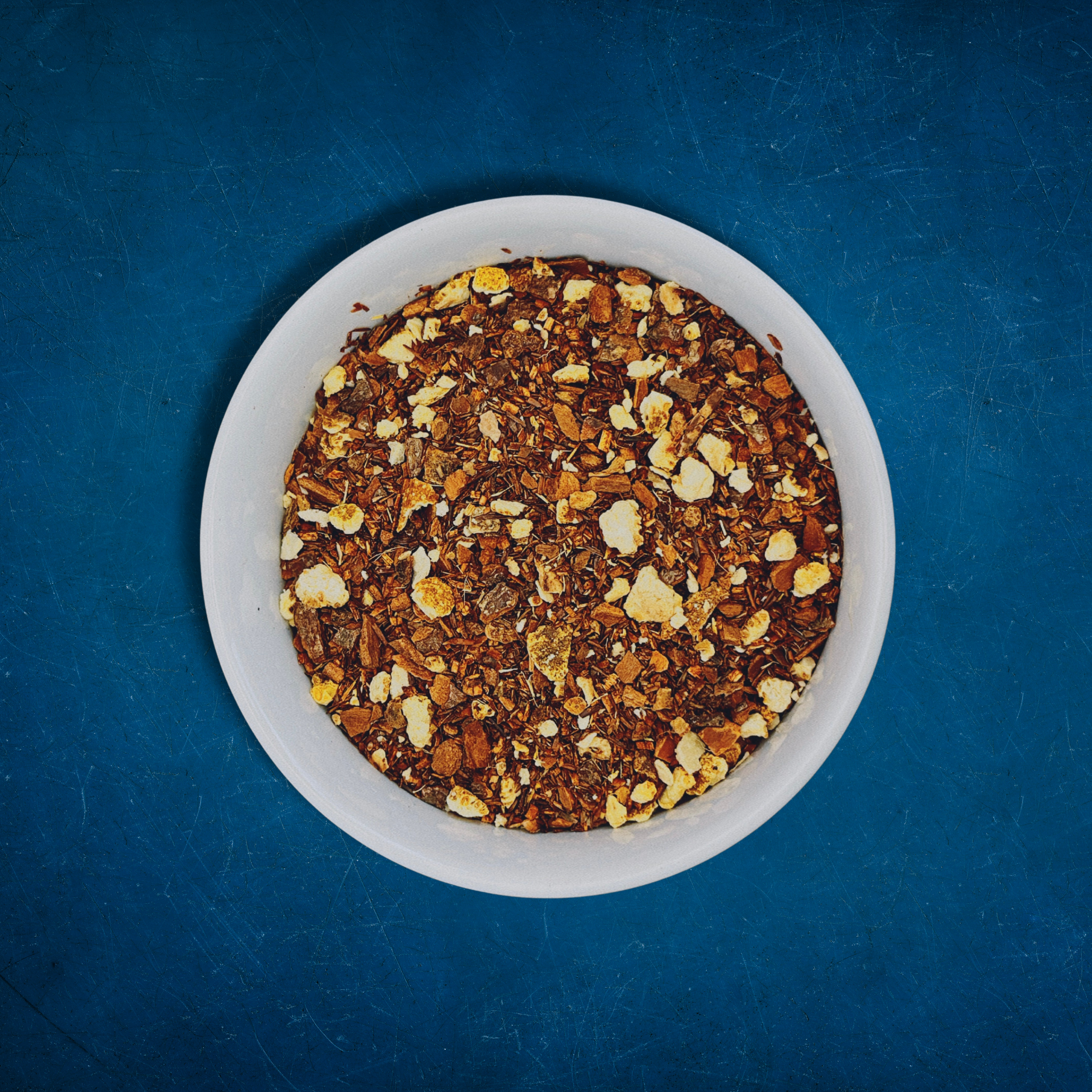Close-up of Sunset Spice loose-leaf Apple Cider Rooibos caffeine-free tea in a white bowl on a blue background by Wonder Waves Coffee