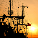 Silhouette of an old pirate ship's masts against a sunset, representing adventure and discovery for Captain's Compass, the 'coffee of the month' subscription
