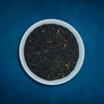 Close-up of Mighty Monarch English Breakfast loose-leaf black tea in a white bowl on a blue background by Wonder Waves Coffee