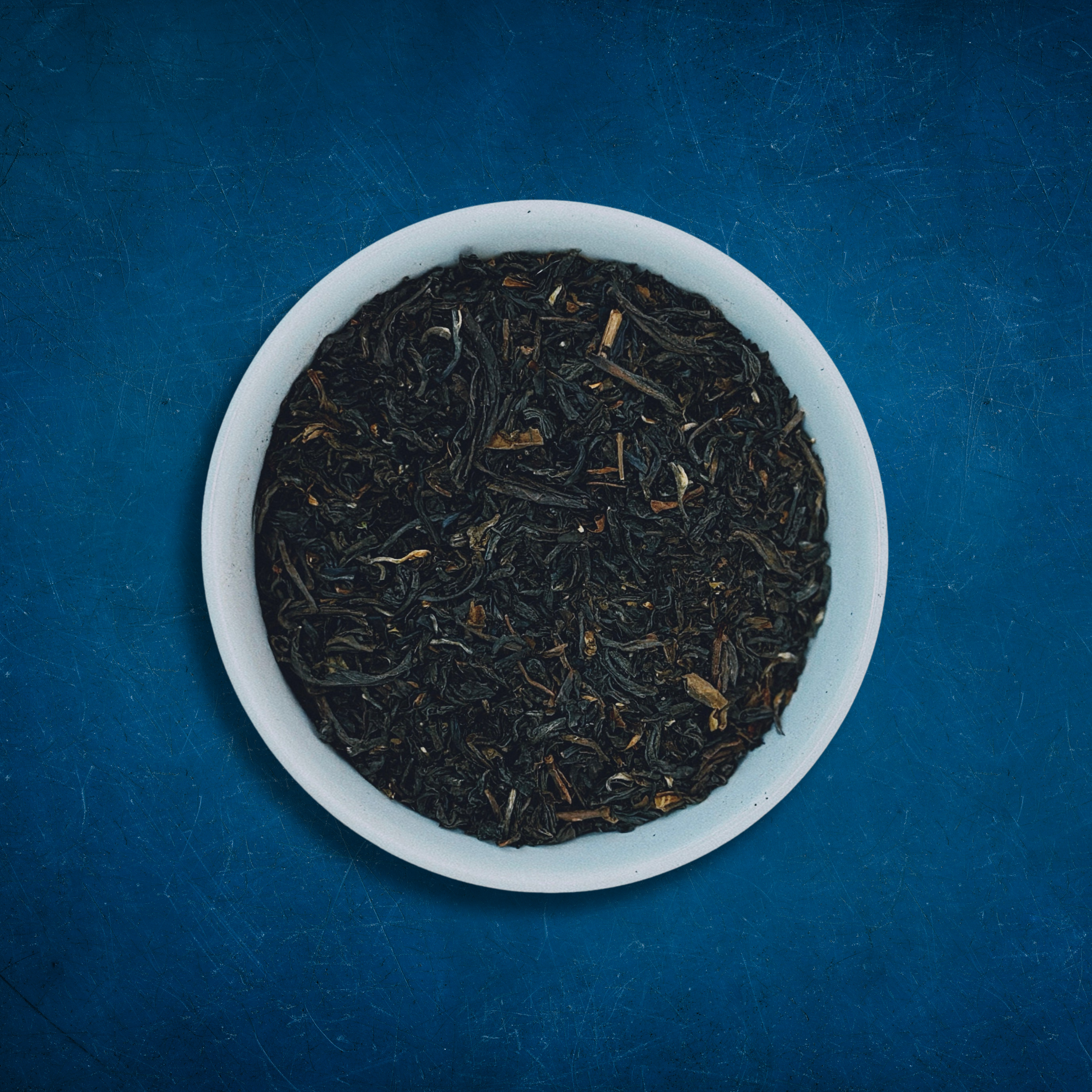 Close-up of Mighty Monarch English Breakfast loose-leaf black tea in a white bowl on a blue background by Wonder Waves Coffee