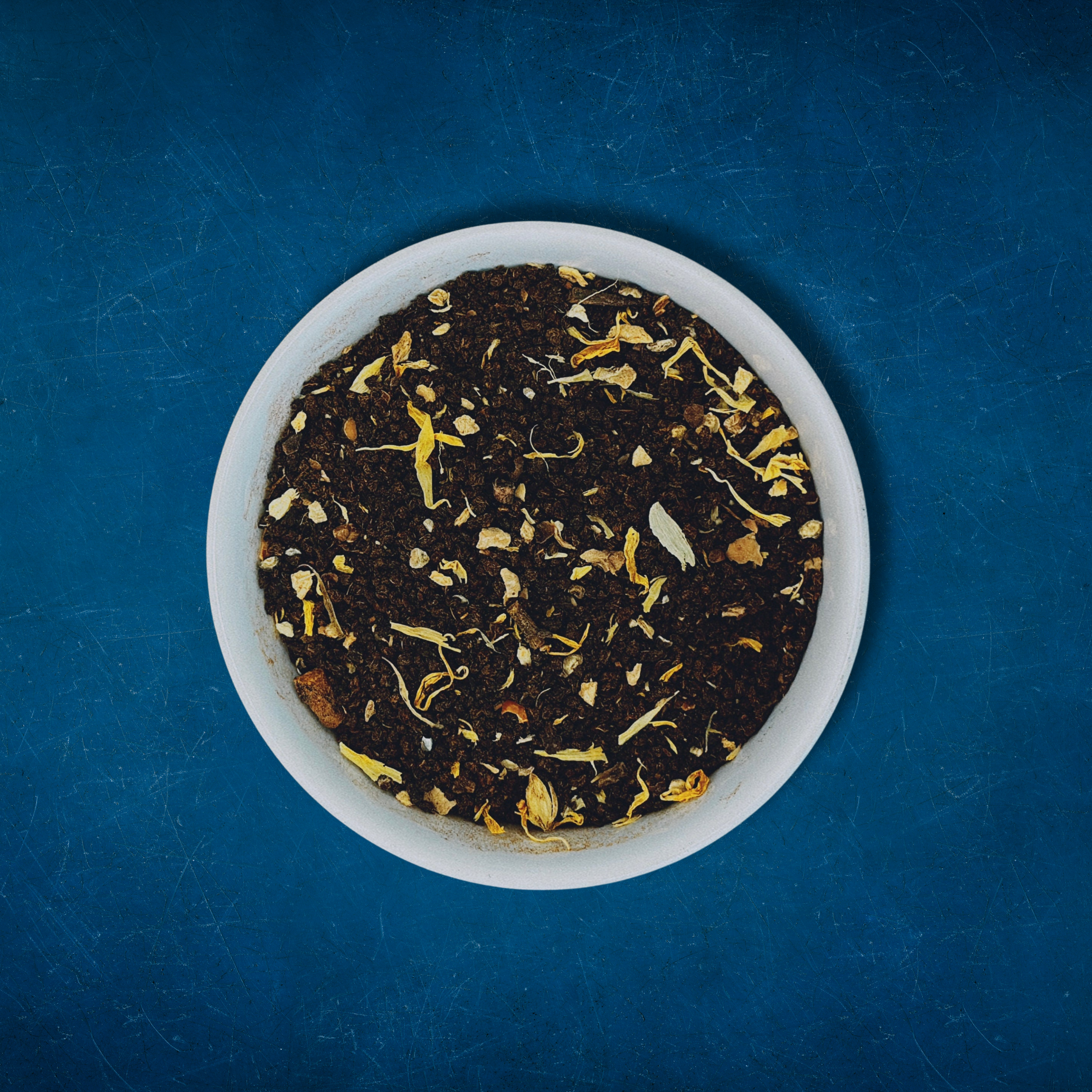 Close-up of Sassy Seagull loose-leaf masala chai black tea in a white bowl on a blue background by Wonder Waves Coffee