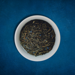 Close-up of Harbor Haze loose-leaf Earl Grey black tea in a white bowl on a blue background by Wonder Waves Coffee