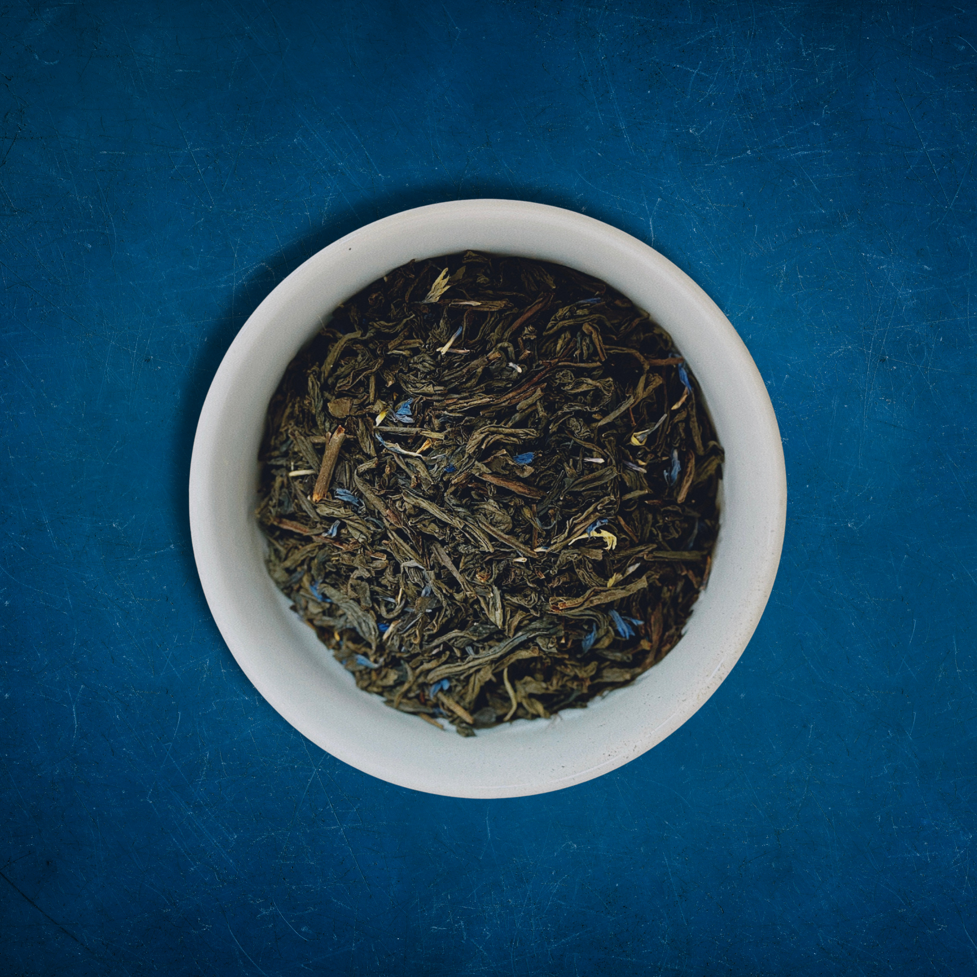 Close-up of Harbor Haze loose-leaf Earl Grey black tea in a white bowl on a blue background by Wonder Waves Coffee