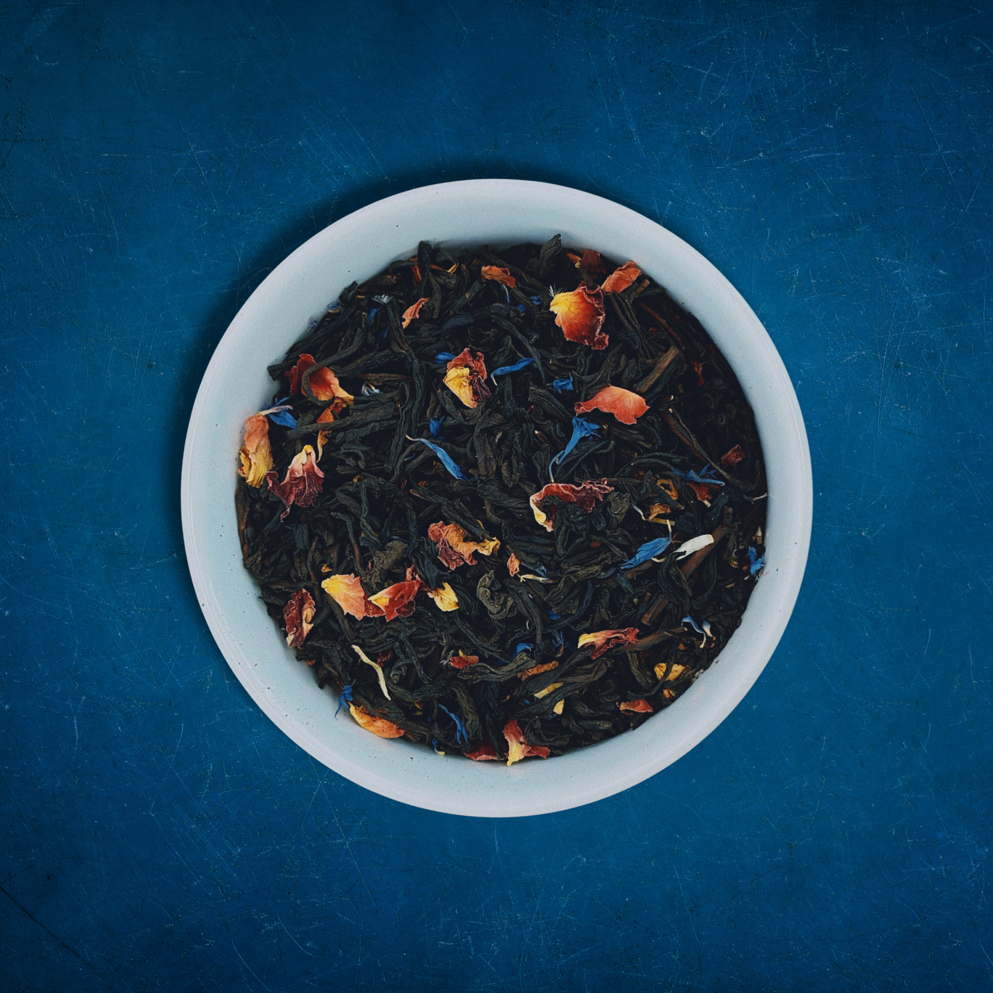 Close-up of Paradise Plunge loose-leaf Peach black tea tea in a white bowl on a blue background by Wonder Waves Coffee