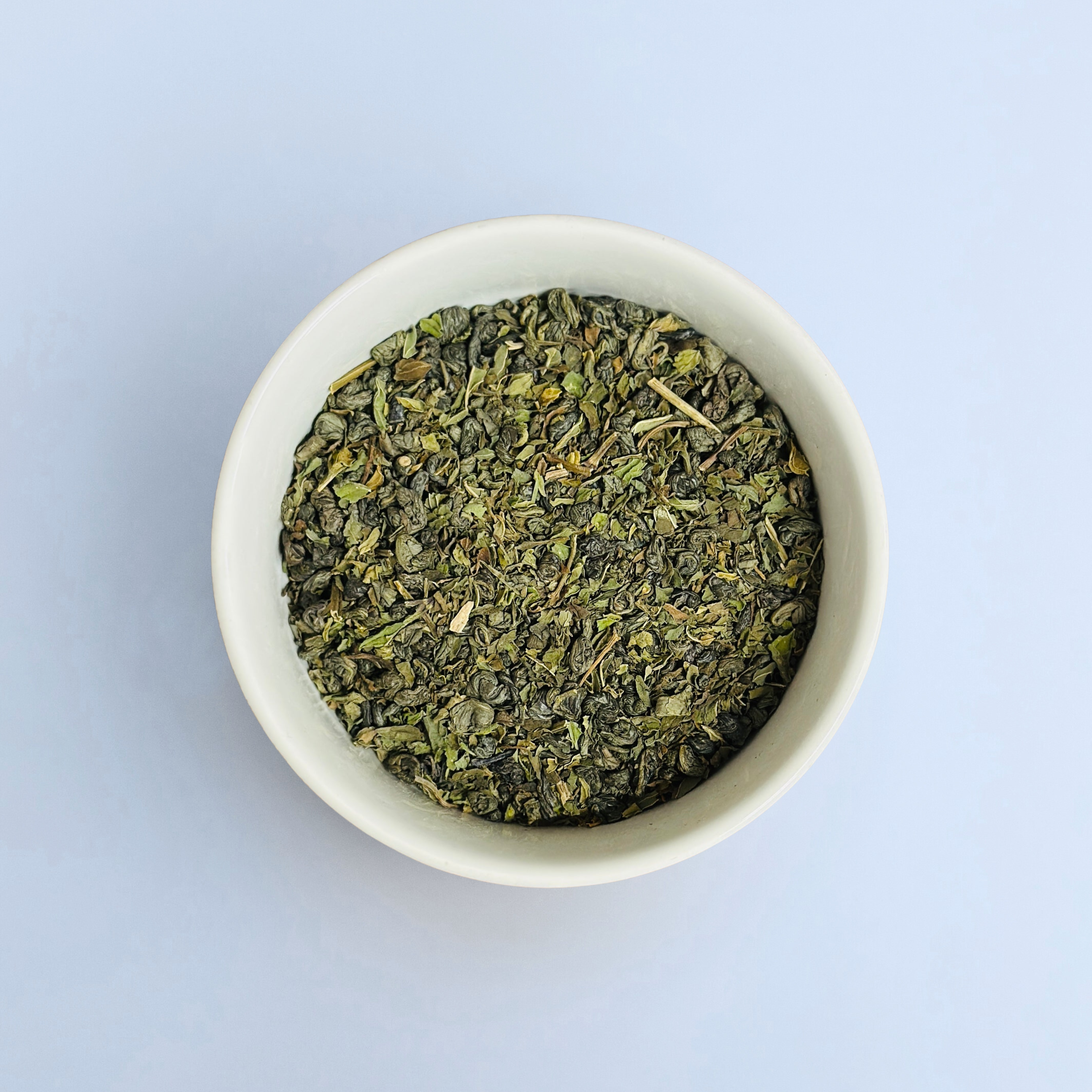 Close-up of Tangier Tingle loose-leaf Moroccan green tea in a white bowl on a white background by Wonder Waves Coffee