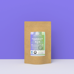 Gulfstream Glow Jasmine Green Tea packaging with a rustic kraft pouch design, featuring a gradient purple-to-green ocean-themed label with jellyfish illustrations, flavor descriptors, and the ‘Artisan Tea’ label. Includes branding for Wonder Waves Coffee, emphasizing its crisp, floral, and earthy profile and eco-friendly packaging.