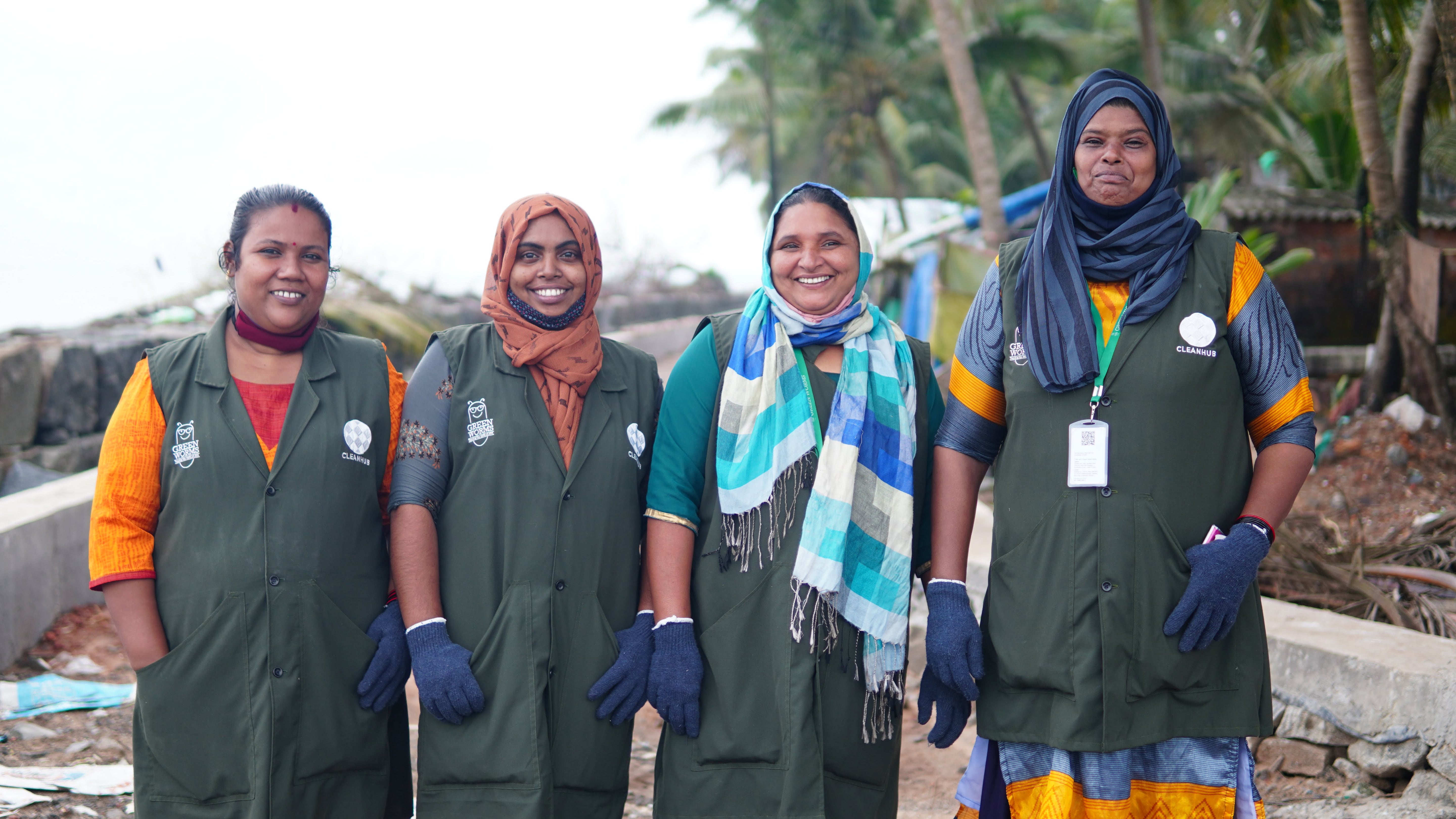 Four CleanHub collection team members smiling in uniform at a coastal cleanup site, representing the human impact behind Wonder Waves Coffee's ocean plastic recovery partnership