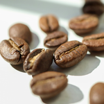 Close-up of specialty roasted coffee beans on a white surface, representing Wonder Waves blend coffee subscription