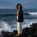 Woman holding coffee while standing on rocky ocean cliffs, capturing the bold, adventurous spirit of Kraken’s Kiss African blend by Wonder Waves Coffee.