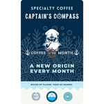 Product label for Wonder Waves Coffee "Captain's Compass" Coffee of the Month subscription. The design features a nautical illustration of a bearded sea captain with a pipe and ship’s wheel against a navy blue coral reef background. Text reads "A New Origin Every Month" and includes the brand mission "Waves of Flavor, Tides of Change."
