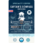 Product label for Wonder Waves "Captain's Compass" Coffee of the Month featuring Costa Rica Coto Brus beans. The navy blue label shows a white sea captain illustration and the Costa Rica flag. It is a medium roast with bright acidity and tasting notes of sweet berry, citrus, and chocolate brownie, grown at 1,200–1,500 MASL.