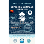 Product label for Wonder Waves Coffee "Captain's Compass" Coffee of the Month featuring Papua New Guinea Jiwaka Province beans. The navy blue label shows a white sea captain illustration and the Papua New Guinea flag. It is a medium roast with medium acidity and tasting notes of blueberry, plum, rose, nutmeg, and chocolate, grown at 1,500–1,700 MASL.