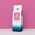 Wonder Waves Coffee Caribbean Coast Colombia 12oz bag. A single origin medium roast coffee with a vibrant pink and tropical wave design featuring a beach hut icon.