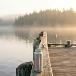 Fisherman's Fuel post roast blend coffee lifestyle image featuring a stainless steel travel bottle on a lakeside dock at sunrise by Wonder Waves Coffee