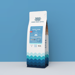 A 12oz bag of Wonder Waves Coffee "Pacific Pearl" single-origin whole bean coffee from the Amazonas region of Peru. The packaging features a clean white top with a teal wave pattern at the base and a blue label illustrating a pearl in a seashell.