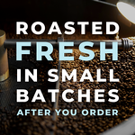 Close-up photograph of a professional industrial coffee roaster with freshly roasted, dark whole beans cooling in the bin, overlayed with bold white and light blue text reading: 'ROASTED FRESH IN SMALL BATCHES AFTER YOU ORDER.'