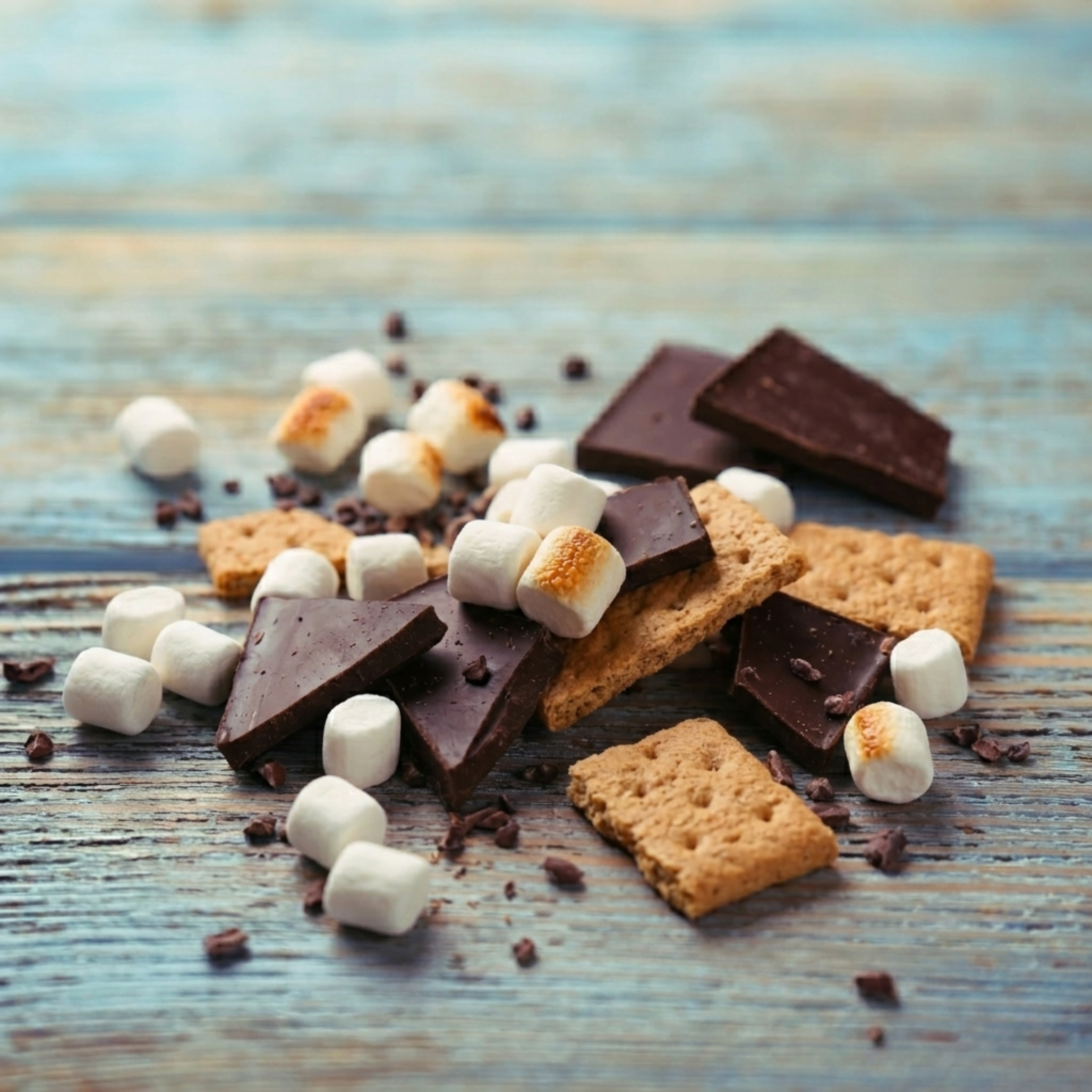 Chocolate, marshmallows and graham crackers on a rustic surface highlighting the rich, sweet and toasted flavor notes of Wonder Waves Coffee Bonfire Bay s’mores flavored coffee.