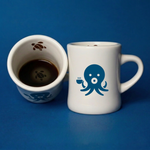 Two Wonder Waves Coffee white ceramic diner mugs on a navy background showing Ollie the Octopus exterior graphic and the hidden sea turtle detail printed inside the mug